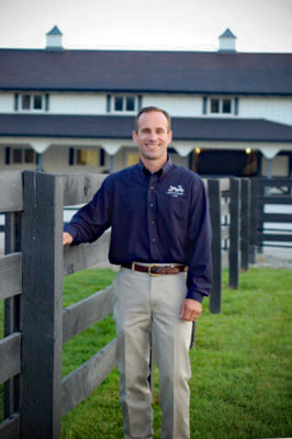 Dr. Scott is standing next to a black fence in front of the Equine Clinic.